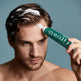 Man applying a green hair growth product to his head with a gray background