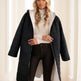 Woman wearing a black puffer coat with a white hood in a bright room.