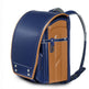 A traditional Japanese-style school backpack in navy blue and tan faux leather, featuring a structured dome shape, front zippered pocket, and padded shoulder straps, shown on a white background.