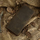 A dark brown leather journal or notebook with visible stitching, placed diagonally on a textured burlap fabric with scattered dried leaves.