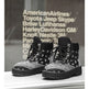 A pair of black and gray lace-up ankle boots with a bandana print pattern, displayed on a white ledge in front of a dark wall with white text.