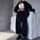 Person wearing a black tracksuit and white crop top in a minimalistic room.