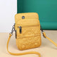 Yellow quilted crossbody bag with braided strap on a beige surface with teal background
