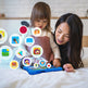 Woman and child playing with a tablet on a bed, surrounded by colorful app icons.