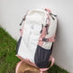 White and pink backpack with visible branding on a grassy surface.