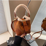 Brown suede handbag with fur trim held by a hand against a neutral background