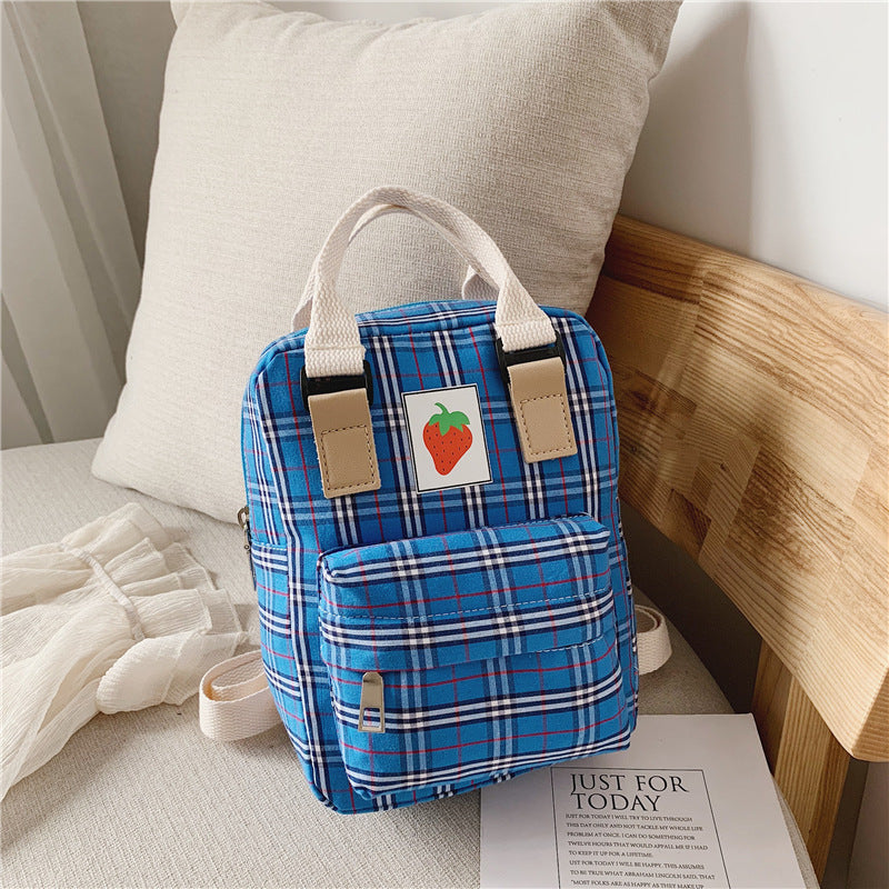 Blue plaid backpack with a strawberry patch logo on a bed