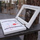 White framed picture with child's drawing leaning against a tree outdoors