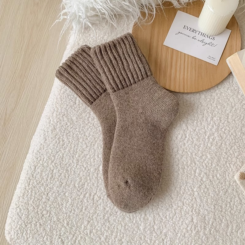 Calze lavorate a maglia marroni su una superficie strutturata con una tavola di legno e un biglietto sullo sfondo.
