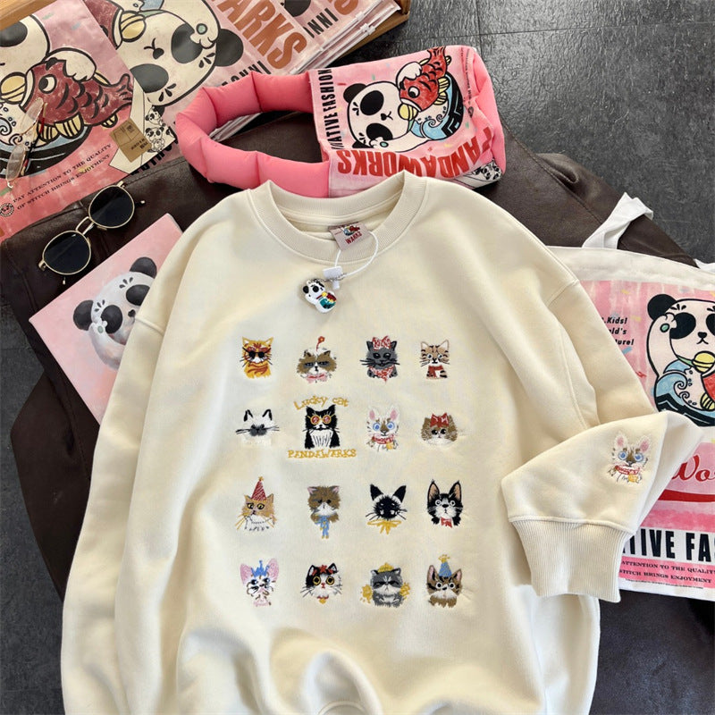 White sweatshirt with cat illustrations on a table with branded products in the background