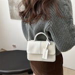 Person wearing a gray sweater holding a white handbag with a visible brand tag.