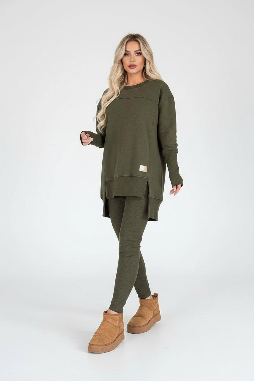 Woman wearing an olive green outfit with a sweater and leggings, standing in a modern interior setting.