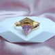 Gold ring with a heart-shaped pink gemstone on a white stand with a pink fabric background