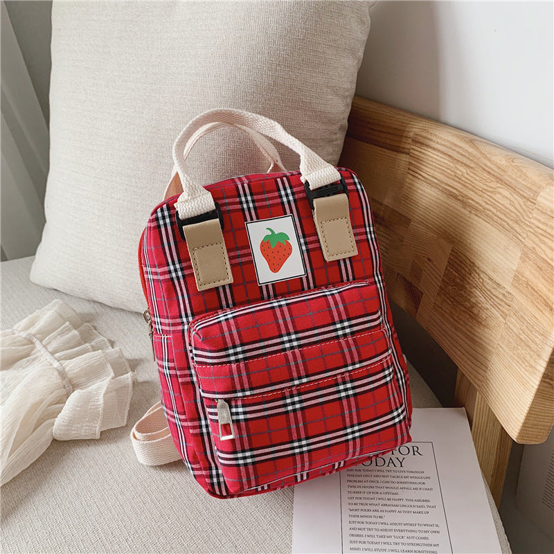 Red plaid backpack with a strawberry design on a light wooden surface