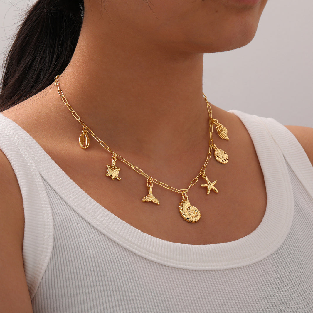 Gold necklace with various charms worn by a person against a neutral background