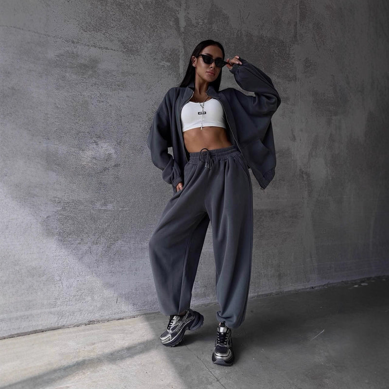 Person wearing a gray tracksuit and white crop top against a concrete wall.