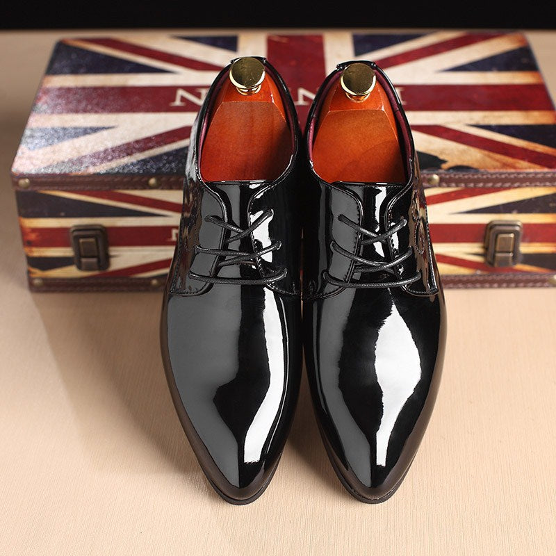 Shiny black dress shoes with gold accents on a beige surface with a Union Jack box in the background.