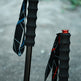 Two hiking poles with textured black grips and wrist straps, one with a blue top cap and one with a red top cap, standing on a gray concrete surface.