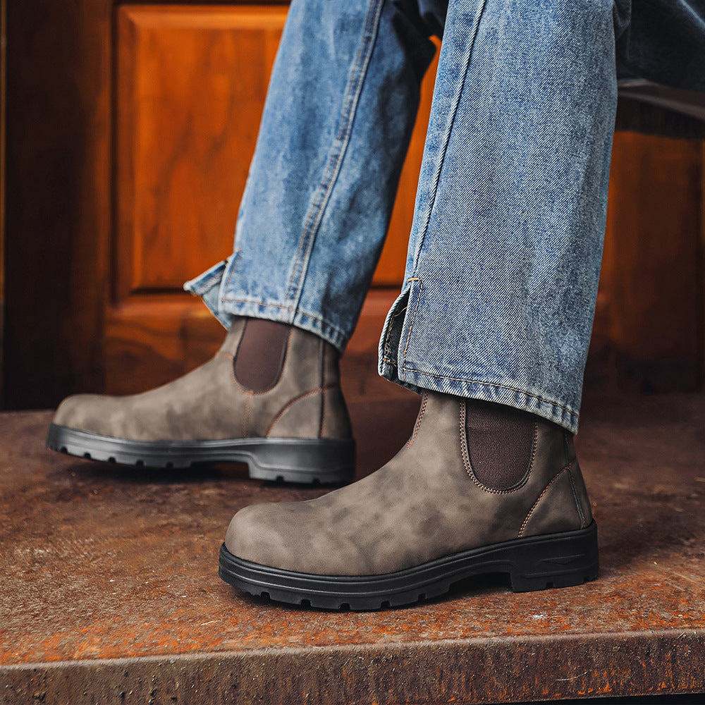 Brown leather boots worn with blue jeans on a wooden floor.