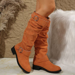 Orange knee-high boots with metal buckles on a textured surface