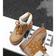 A pair of brown ankle boots with white bandana print overlays, brown laces, and white cuffs, displayed on a white geometric platform against a dark textured background.