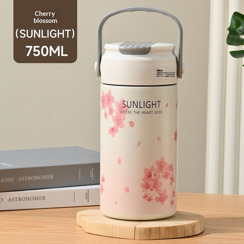 Thermos with cherry blossom design on a wooden surface with books in the background