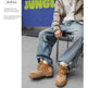 A person seated on a stool wearing tan lace-up boots with a white bandana pattern, light blue ripped jeans, a white T-shirt, and a beige zip-up hoodie. The photo is styled like a magazine fashion editorial with a blue background and the word 'JUNGLE' visible.