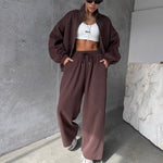 Person wearing a brown tracksuit and white crop top against a gray wall.