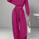 Person wearing a magenta outfit with wide-leg pants and a matching top, holding a white handbag on a gray background.