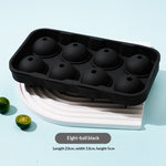 Black silicone ice cube tray with eight dome-shaped cavities, shown on a white curved stand against a light blue background with small lime slices and product text overlay.