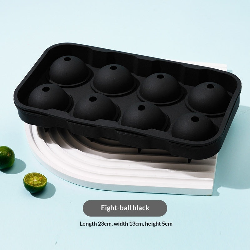 Black silicone ice cube tray with eight dome-shaped cavities, shown on a white curved stand against a light blue background with small lime slices and product text overlay.