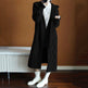 Person wearing a long black coat with a plain background