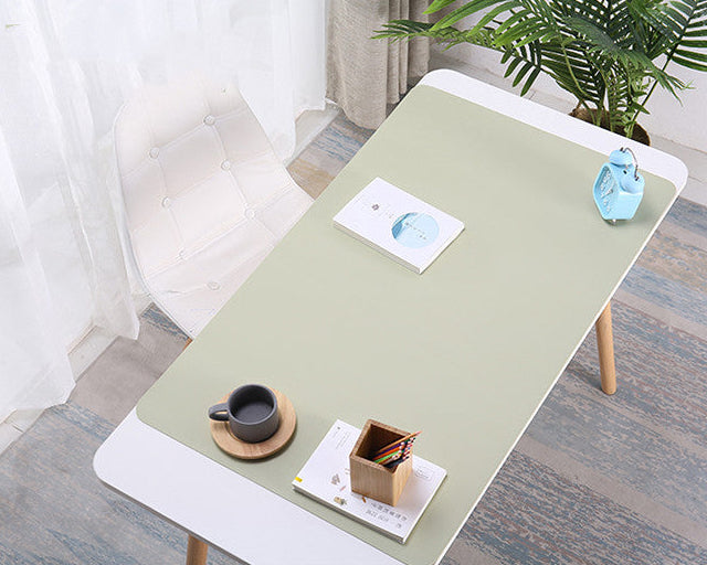 Light green desk pad on a wooden desk with a cup, saucer, and small plant in a room.