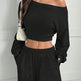 Person wearing a black off-shoulder top and black pants against a white wall.