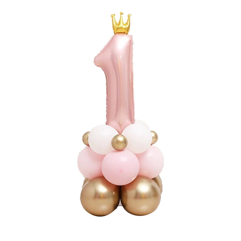 Pink balloon sculpture shaped like the number '1' with a gold crown on top, surrounded by smaller balloons.