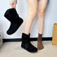Person wearing black boots with one boot being held up, on a plain floor background.