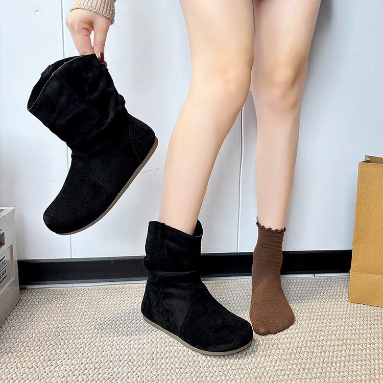 Person wearing black boots with one boot being held up, on a plain floor background.
