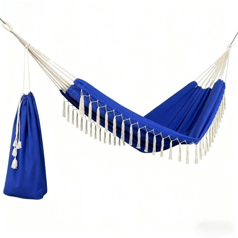 A royal blue hammock with white rope suspension and tassels, shown on a plain white background alongside a matching blue drawstring storage bag.