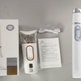 Dispositivo White Beauty Wand mostrato con la sua confezione al dettaglio, cavo di ricarica e manuale d'istruzioni su uno sfondo grigio chiaro.