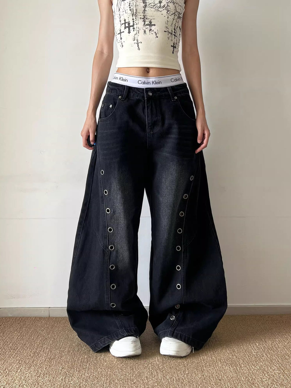 Person wearing wide-leg dark jeans with button details on a plain background