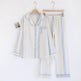 A two-piece cotton pajama set consisting of a long-sleeve button-up shirt and matching pants, hanging on wooden hangers against a plain white background. The pajamas feature a textured gauze-like fabric with vertical stripes in cream, light blue, and white, accented with light blue piping.