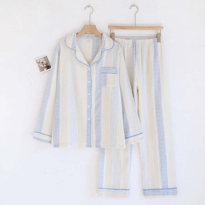 A two-piece cotton pajama set consisting of a long-sleeve button-up shirt and matching pants, hanging on wooden hangers against a plain white background. The pajamas feature a textured gauze-like fabric with vertical stripes in cream, light blue, and white, accented with light blue piping.