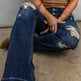 Person wearing a brown ribbed tank top and blue distressed jeans sitting on the floor.