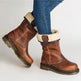 A pair of brown leather ankle boots with a cream-colored faux fur collar, shown on a model wearing blue jeans against a plain white background.