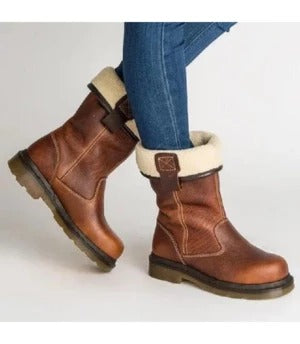 A pair of brown leather ankle boots with a cream-colored faux fur collar, shown on a model wearing blue jeans against a plain white background.