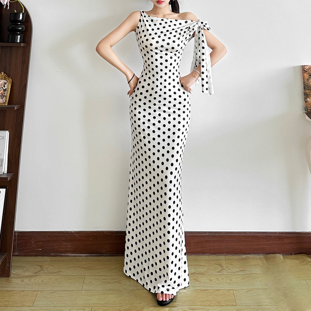 Woman wearing a polka dot dress standing against a plain wall.
