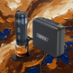 A black Hibrew portable espresso maker with a glass cup under the nozzle, shown next to its matching black carrying case on a textured, abstract brown and gold paint background.