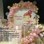 Pink and gold balloon decoration set for a child's birthday party, featuring a large arch backdrop with a cartoon girl illustration and the text 'Maria Alice', plus matching balloon garlands and floral arrangements.