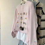 Pink sweatshirt with embroidered designs on a hanger against a neutral background