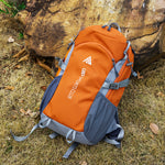 Orange and gray backpack with visible branding on a grassy ground with rocks.